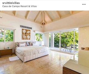 A bedroom with a large bed, a nightstand, a desk, and a window with a view of greenery. - Snrvittinivillas Mng Spacius and Best Loc in Casa de Campo Resorts Gr8 Villa (La Romana)