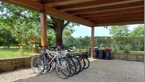 A covered outdoor area with bicycles parked under a wooden structure, surrounded by gravel and greenery.