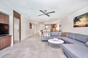 A modern living room with a grey sectional sofa, a flat-screen TV, a ceiling fan, and a dining area in the background.