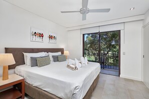 Un dormitorio con una cama grande, dos obras de arte en la pared, un ventilador de techo y un ventanal corredero que da a un área exterior.