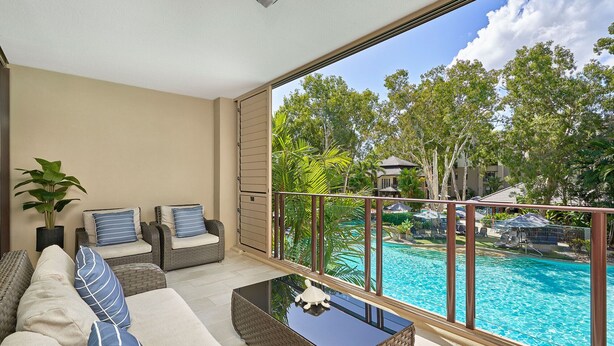 Un balcón con vistas a una piscina, muebles de mimbre y una lámpara de techo.
