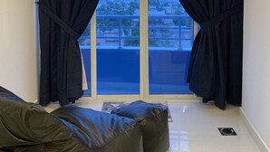 Une chambre moderne dotée d’une grande porte-fenêtre coulissante, de rideaux noirs, d’un canapé en cuir noir et d’une petite table.