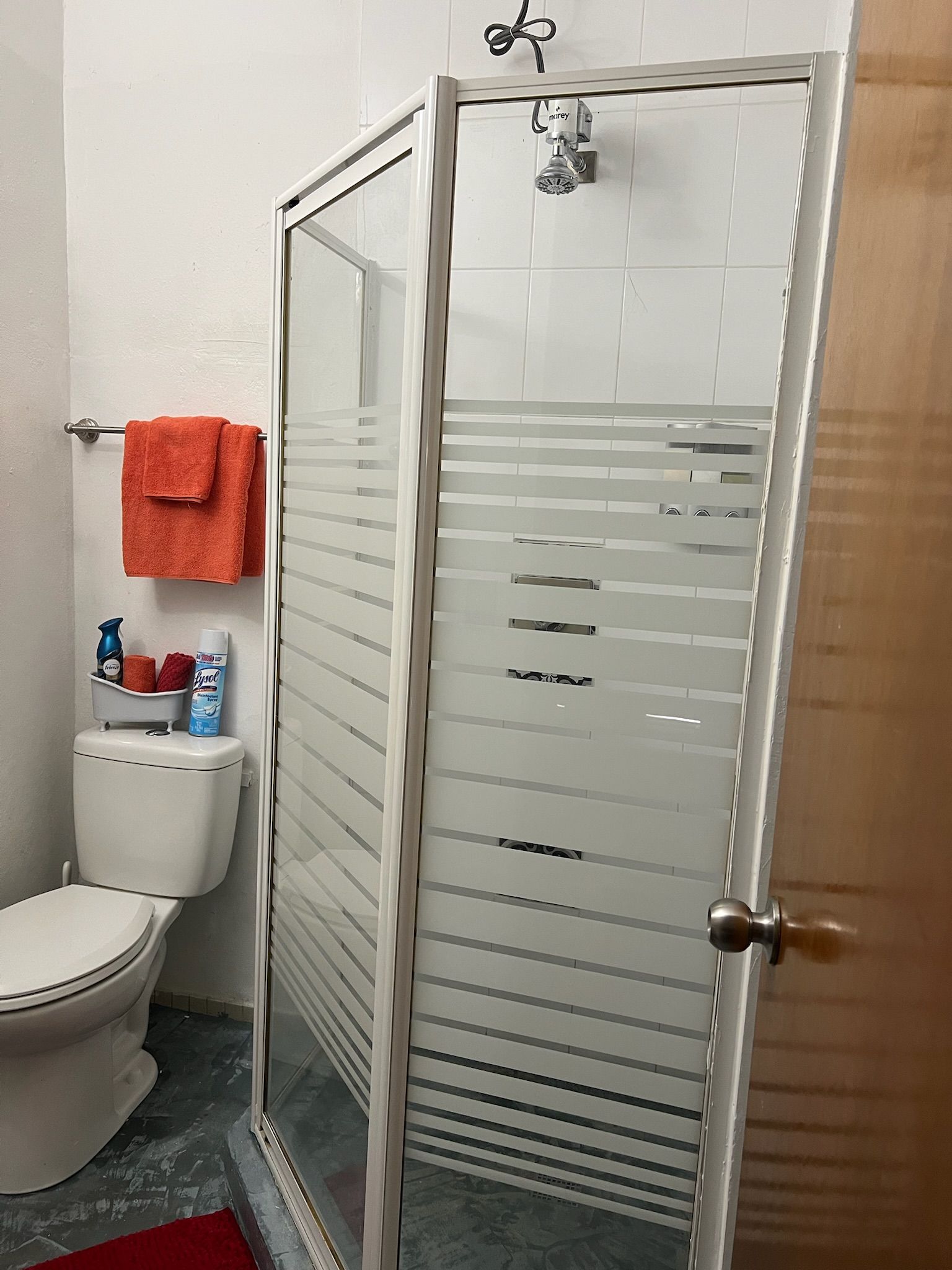 A bathroom with a glass shower enclosure, a toilet, and a towel rack with a red towel.
