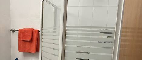 A bathroom with a glass shower enclosure, a toilet, and a towel rack with a red towel.