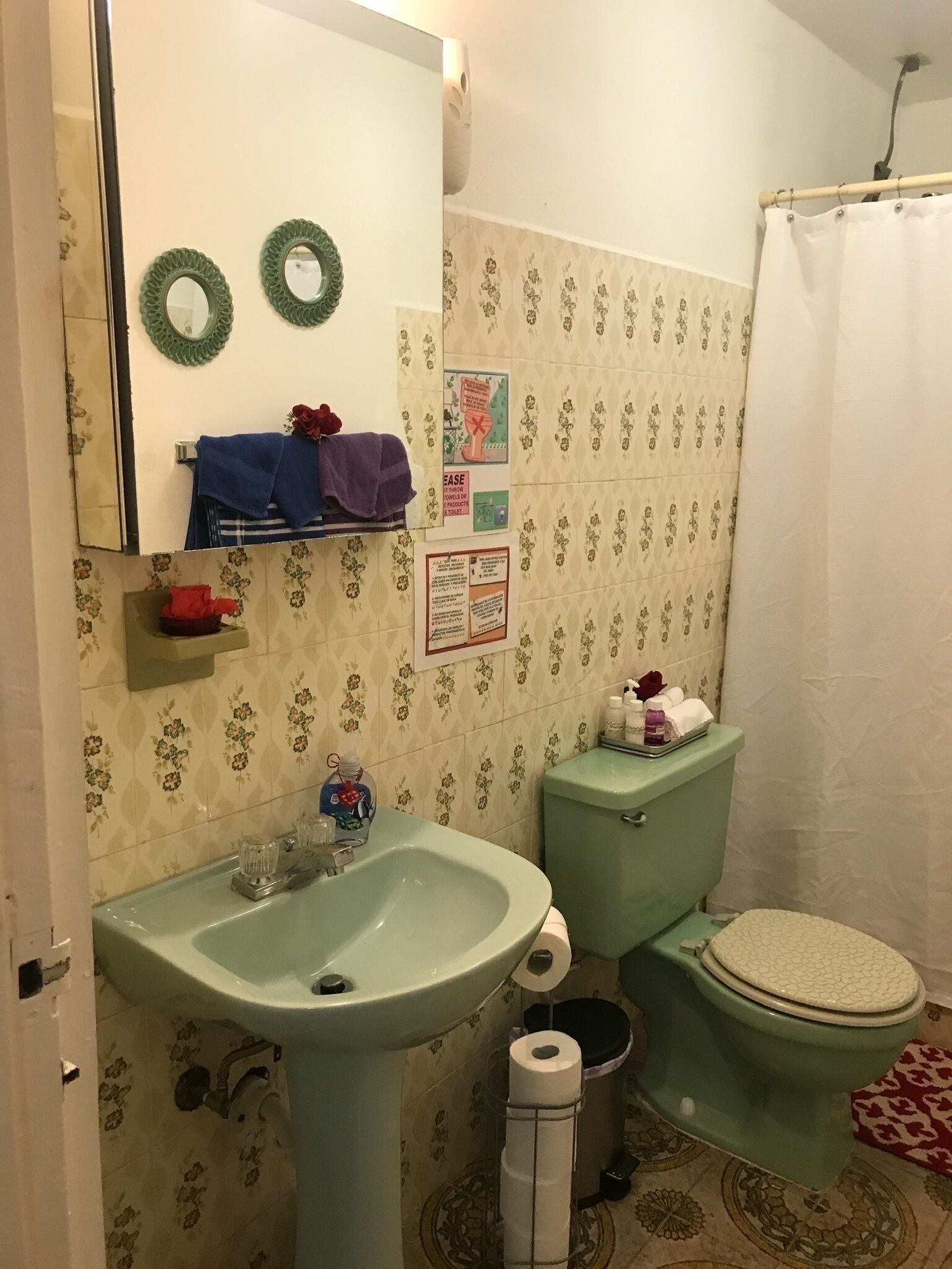 A bathroom with a green sink, toilet, and shower curtain. There are two green wall decorations and a towel rack with towels.
