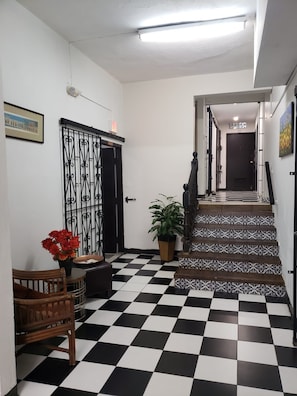 A hallway with a checkered floor, a staircase with patterned tiles, a door with a metal gate, and a potted plant. - 310Guest-House LaVida (San Juan)