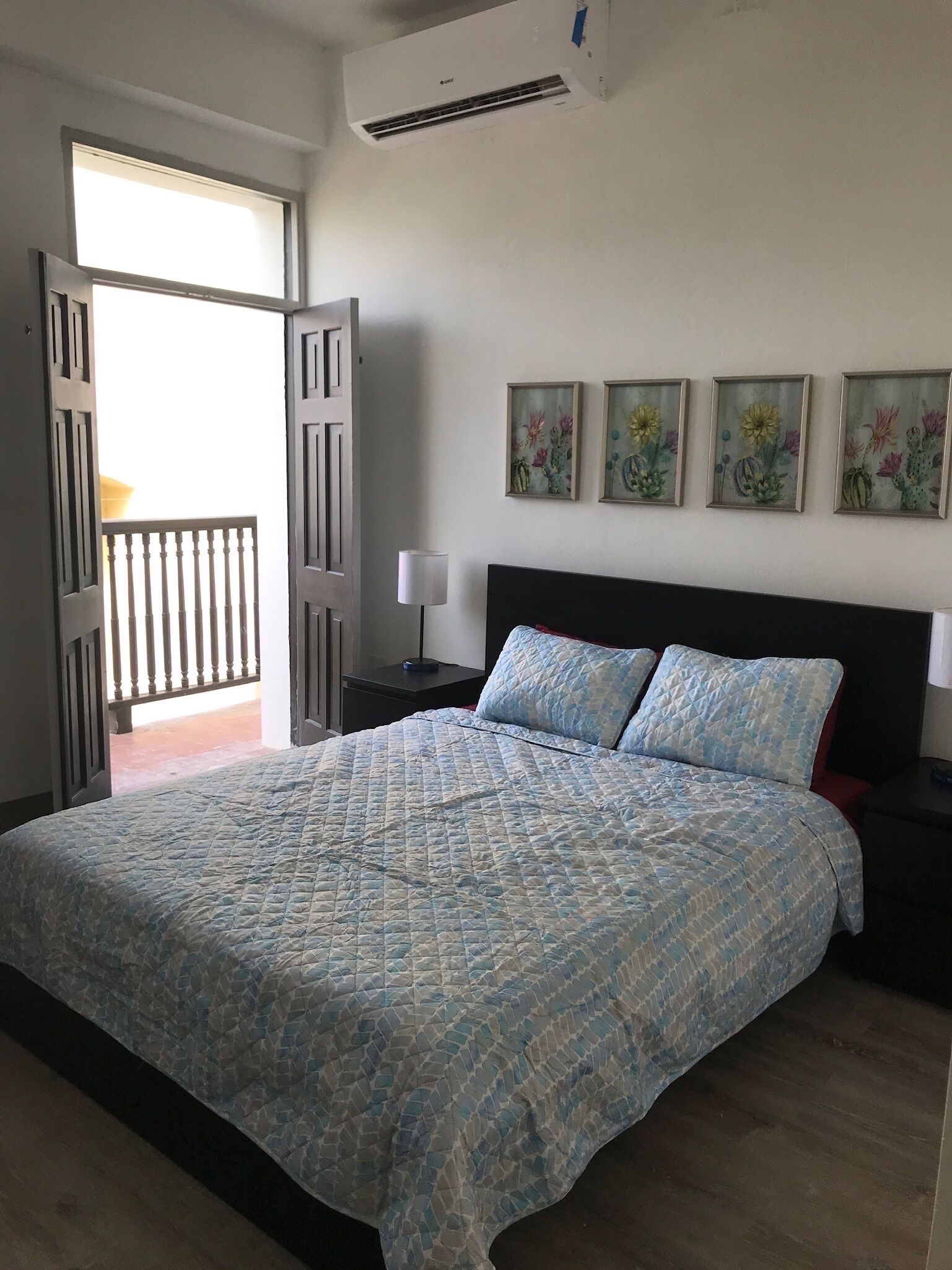 Un dormitorio con una cama grande, una mesita de noche, una lámpara y una ventana con vistas a un balcón.