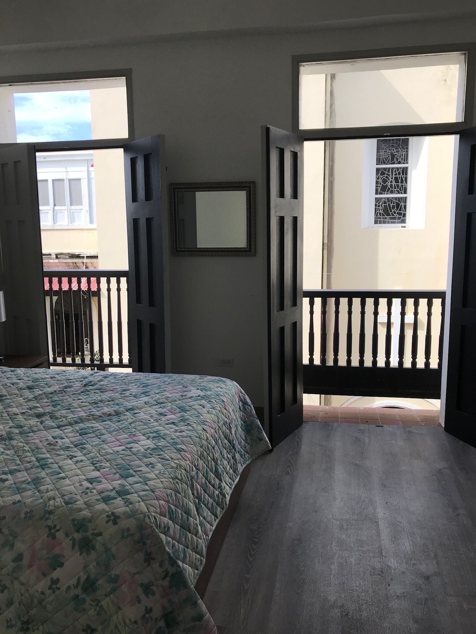 Ein Zimmer mit Bett, Fenster und einer Tür, die auf einen Balkon im Freien führt.