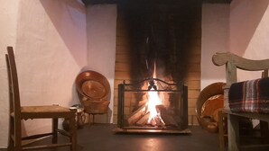 A cozy room with a fireplace, a wooden chair, a bench, and a small table. - Comfort and Serenity in a Typical Alentejo House. (Monte da Pedra)