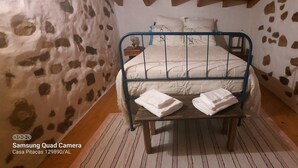 A bedroom with a bed, pillows, a nightstand, and a wooden table with towels. - Comfort and Serenity in a Typical Alentejo House. (Monte da Pedra)