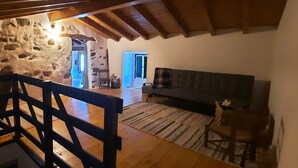 A rustic room with a stone wall, wooden beams, a sofa, and a chair. - Comfort and Serenity in a Typical Alentejo House. (Monte da Pedra)