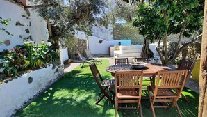 A patio with a round table and chairs, surrounded by greenery and a white wall. - Comfort and Serenity in a Typical Alentejo House. (Monte da Pedra)