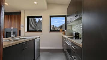 Een moderne keuken met donkere kastjes, een roestvrijstalen spoelbak en een raam met uitzicht op een woning.