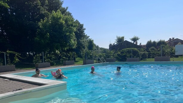 A swimming pool with clear blue water, surrounded by trees and a brick wall. - Apartment In Residence In Porto Levante Ro (Porto Viro)
