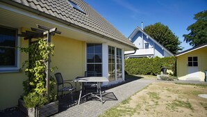Ein gelbes Haus mit Ziegeldach, einer Terrasse mit Tisch und Stühlen sowie einem Garten.