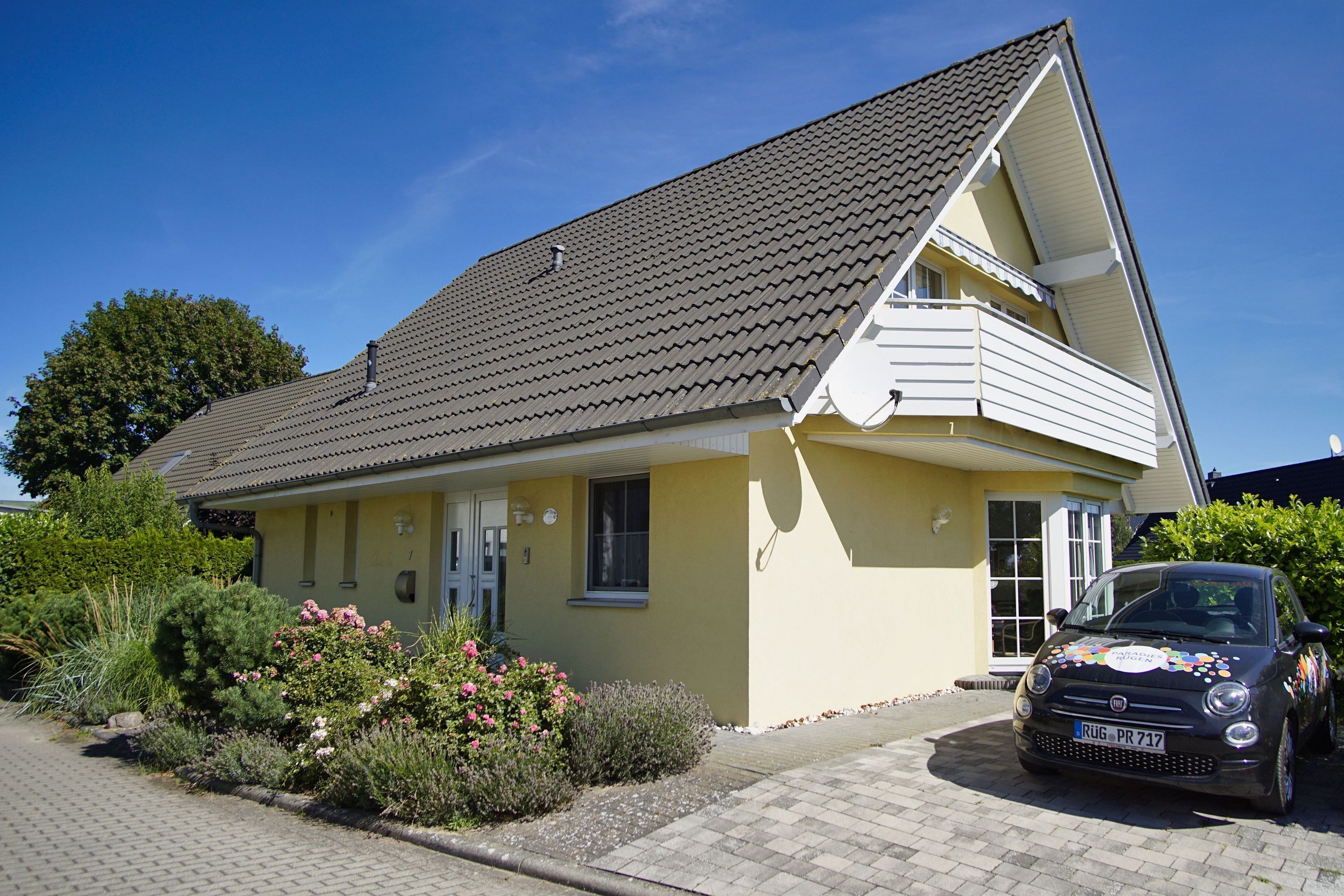 Ein zweistöckiges Haus mit Ziegeldach, einem Balkon und einem geparkten Auto davor.