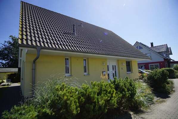 Un bâtiment jaune avec un toit recouvert de tuiles, une porte et des fenêtres.