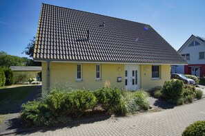 Un bâtiment jaune avec un toit en tuiles, un petit jardin devant et une allée pavée.
