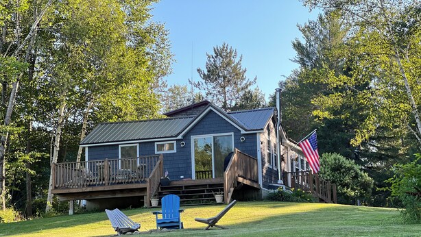 En hytte med terrasse, en blå Adirondack-stol og et amerikansk flag.