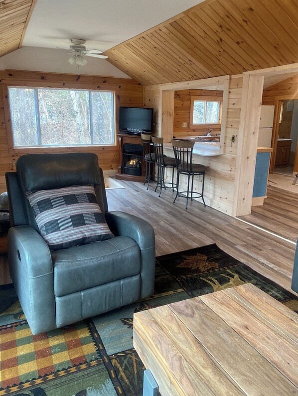 A cozy cabin interior with a leather recliner, a fireplace, a dining area, and a television.
