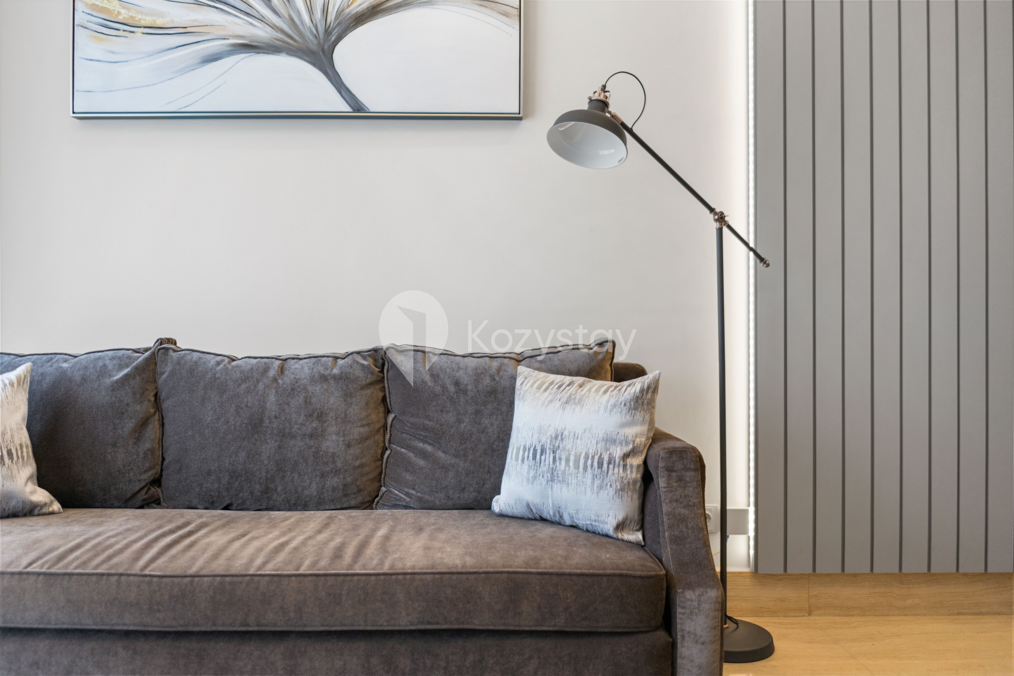 A modern living room with a grey sofa, a floor lamp, and a vertical blinds panel.