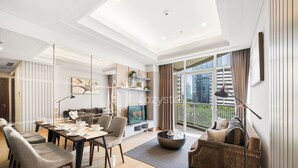 A modern living room with a dining area, a sofa, a coffee table, a TV, and a balcony with a view of the city. - EBONY by Kozystay (Jakarta)