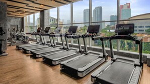 A gym with treadmills aligned against a wall with large windows overlooking a cityscape. - EBONY by Kozystay (Jakarta)