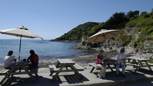 Ett område vid stranden med picknickbord och parasoller, med utsikt över havet.
