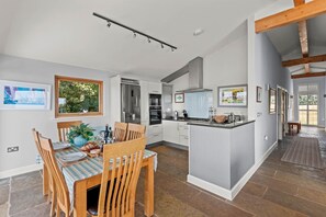 A modern kitchen with a central island, built-in appliances, and a dining area with wooden furniture. - House 38 - sleeps 6 guests in 3 bedrooms (Looe)