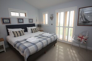 A bedroom with a large bed, a chair, and a painting on the wall. - House 38 - sleeps 6 guests in 3 bedrooms (Looe)