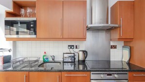 Une cuisine avec des armoires en bois, une hotte de cuisinière en acier inoxydable, un four à micro-ondes, un grille-pain et une bouilloire posés sur le plan de travail.