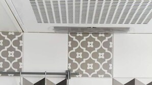 Een keuken met een achterwand van geometrische tegels, een roestvrijstalen afzuigkap en hangende keukengerei.