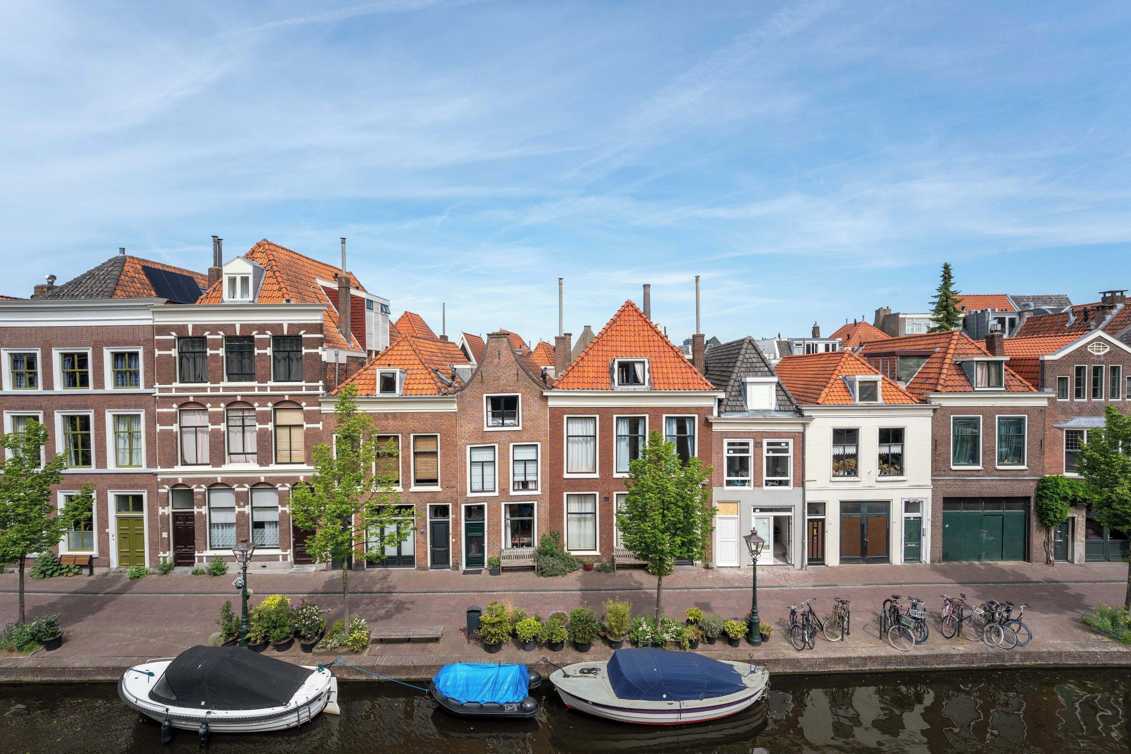A row of traditional European-style buildings with red-tiled roofs, a canal with boats, and bicycles parked along the sidewalk.