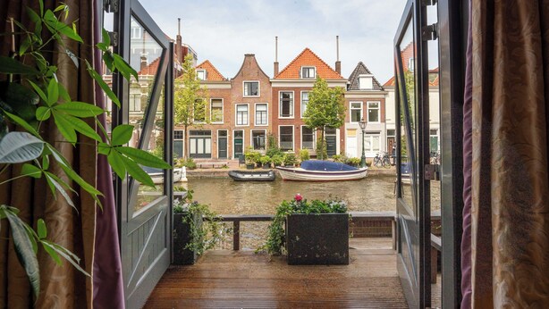 A view from a balcony overlooking a canal with traditional buildings, a boat, and a bicycle. - Pakasa Leiden (Leiden)