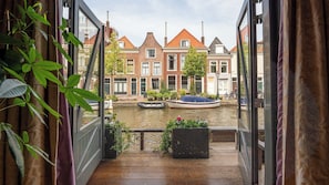 A view from a balcony overlooking a canal with traditional buildings, a boat, and a bicycle. - Pakasa Leiden (Leiden)