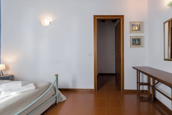 A bedroom with a bed, bedside table, and a door leading to another room.