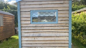 Una cabaña de madera pequeña con una ventana y una escalera de metal al frente.