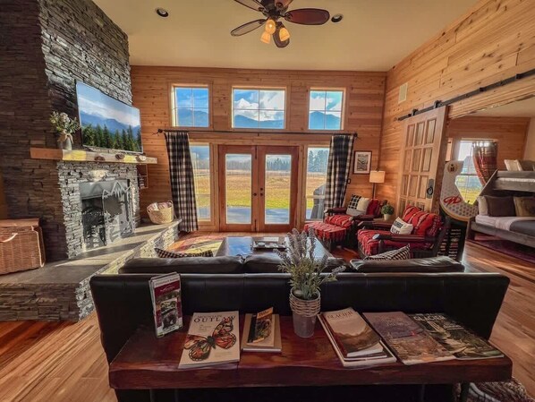A cozy living room with a stone fireplace, a large window with a view, and a comfortable seating area.