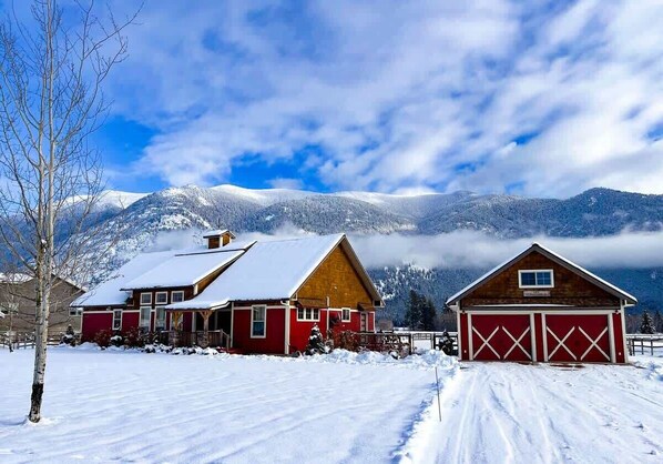 A snow-covered landscape with two red buildings, one with a wooden facade and the other with a red garage.