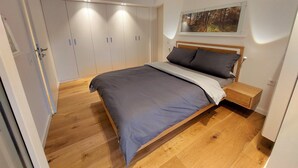 Ein Schlafzimmer mit Bett, Holzboden, Kleiderschrank, Nachttisch und einem Bild an der Wand.