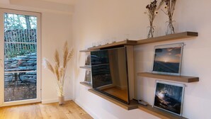 Ein modernes Zimmer mit großem Fenster, Holzboden und einem an der Wand befestigten TV-Regal mit drei gerahmten Bildern.