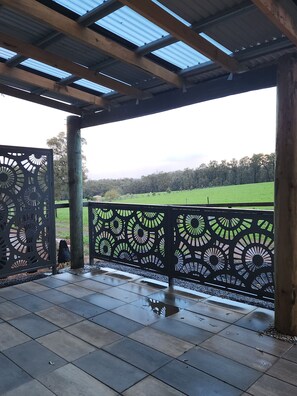 Un espace extérieur abrité, doté d’une clôture en métal à motifs, d’un sol carrelé et offrant une vue sur un champ verdoyant.