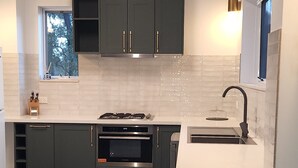 Una cocina moderna con armarios oscuros, horno de acero inoxidable y encimera blanca.
