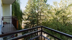 A balcony with a view of a dense forest and a building in the background.