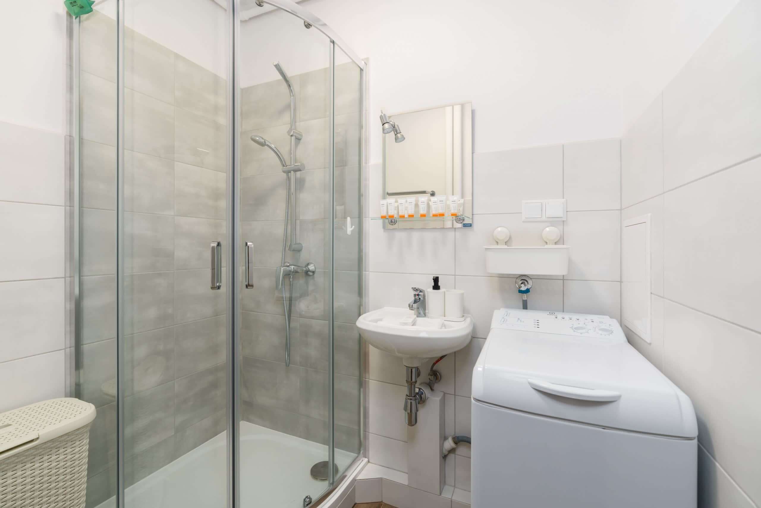 Ein modernes Badezimmer mit einer gläsernen Duschkabine, einem weißen Waschbecken, einem Spiegel und einer weißen Waschmaschine.