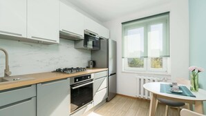 A modern kitchen with a gas stove, oven, and microwave, a dining area with a table and chairs, and a window with a view of greenery.
