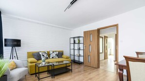 A modern living room with a sofa, coffee table, and a TV. There is a wooden door leading to another room.
