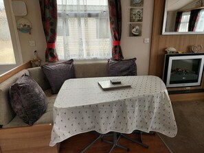 A cozy living room with a sofa, a table with a white tablecloth, a television, and decorative items on the wall.