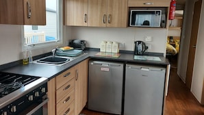 A compact kitchen with wooden cabinets, a stove, a microwave, and a dishwasher. - Cozy Coastal Retreat in Brean (Burnham-on-Sea)