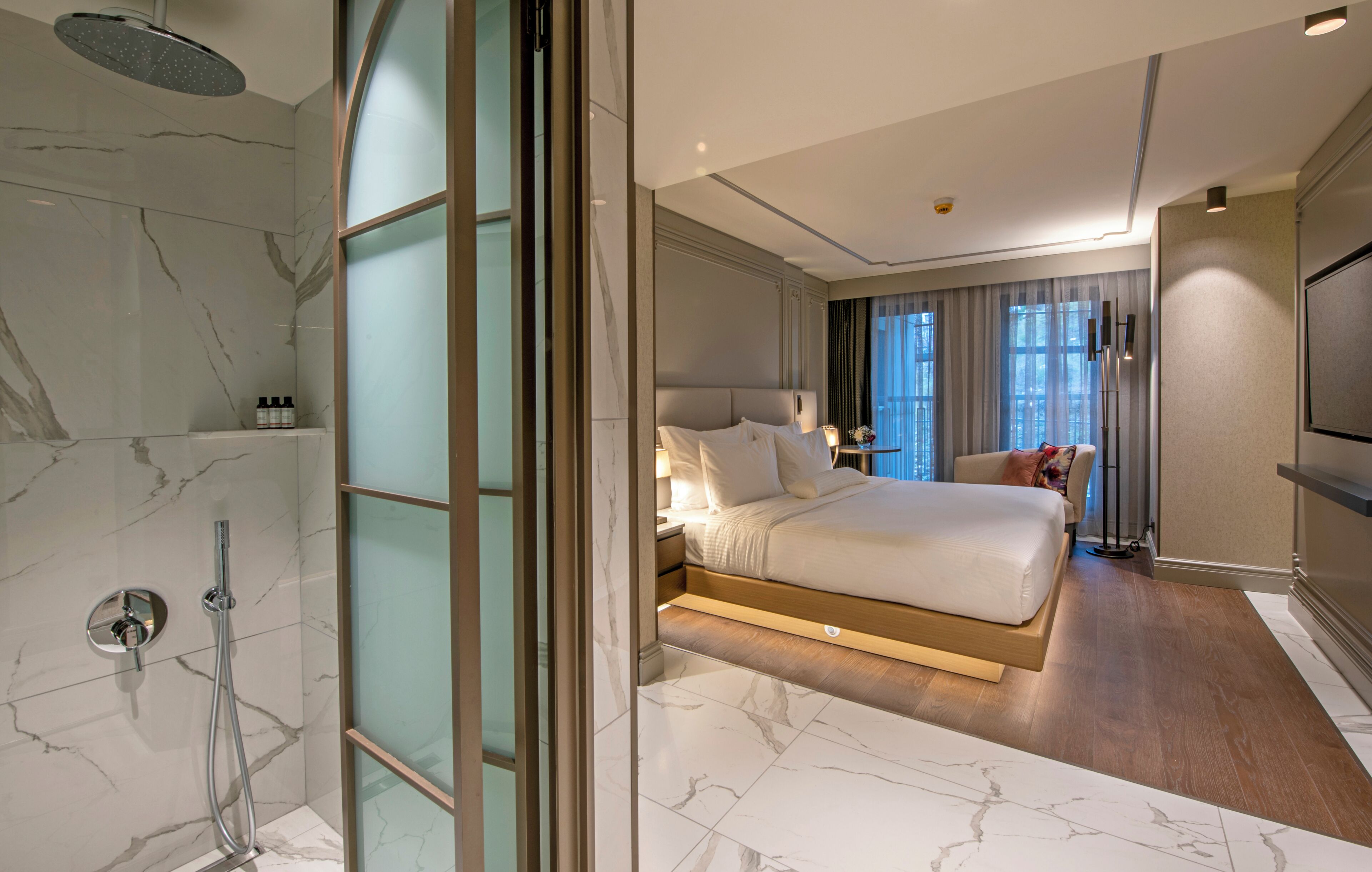A modern hotel room with a marble bathroom, a large bed, a TV, and a view of the city.